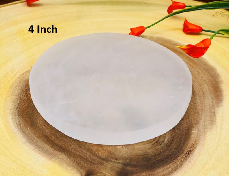 May include: A 4 inch white selenite charging plate. The plate is round and smooth, and it is sitting on a wooden surface.