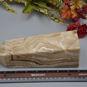 May include: A beige onyx obelisk with brown and white veining. The stone has a rectangular base and a slanted top. A ruler is placed in front of the obelisk. The obelisk is approximately 8 inches long.