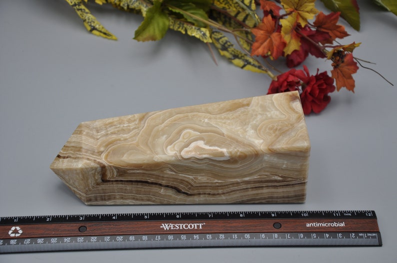 May include: A beige onyx obelisk with brown and white veining. The stone has a rectangular base and a slanted top. A ruler is placed in front of the obelisk. The obelisk is approximately 8 inches long.