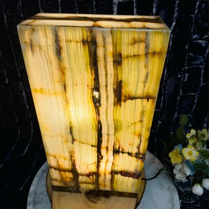 May include: A rectangular, green and yellow onyx lamp with a wood base. The lamp is lit and the light shines through the onyx, creating a warm glow.