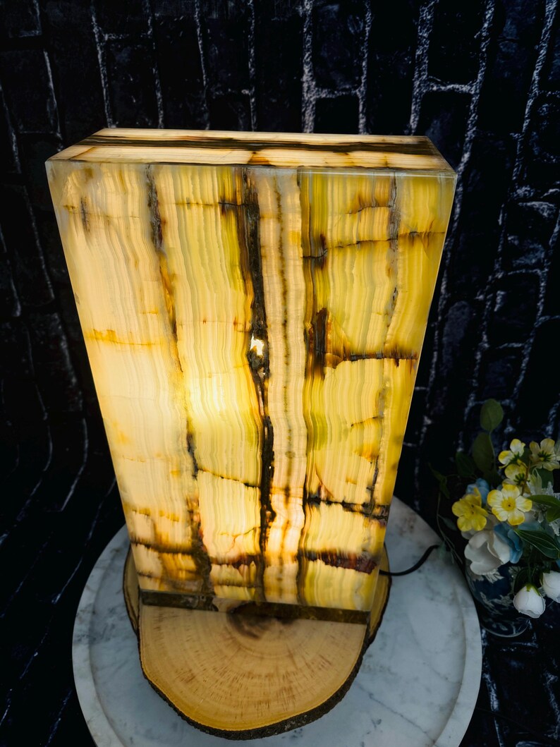 May include: A rectangular, green and yellow onyx lamp with a wood base. The lamp is lit and the light shines through the onyx, creating a warm glow.