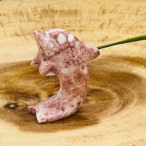 Puede incluir: Una figurita de delf&iacute;n de m&aacute;rmol rosa y blanco tallada a mano. El delf&iacute;n est&aacute; en una pose de salto con la cola curvada hacia arriba.
