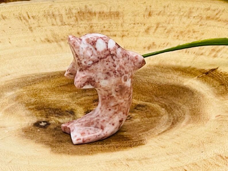 Puede incluir: Una figurita de delf&iacute;n de m&aacute;rmol rosa y blanco tallada a mano. El delf&iacute;n est&aacute; en una pose de salto con la cola curvada hacia arriba.