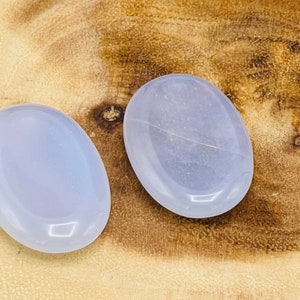 May include: Two light blue oval-shaped polished stones on a wooden surface.
