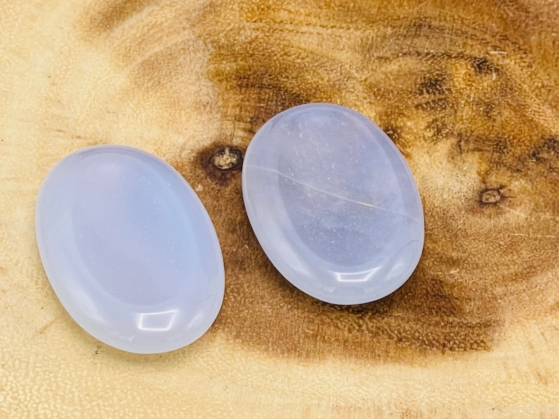 May include: Two light blue oval-shaped polished stones on a wooden surface.