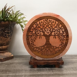 May include: A round Himalayan salt lamp with a carved wooden tree of life design. The lamp is on a wooden base.