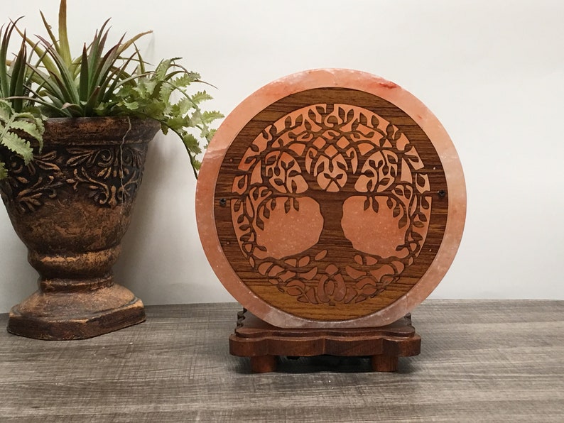 May include: A round Himalayan salt lamp with a carved wooden tree of life design. The lamp is on a wooden base.