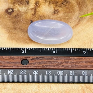 May include: A pale lavender oval-shaped polished stone, approximately 4 inches long, resting on a wooden surface.
