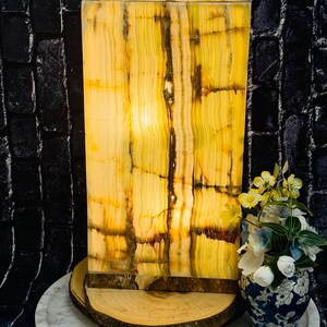 May include: A rectangular, yellow and green onyx lamp with a warm, glowing light. The lamp is sitting on a wooden base and a white marble surface.