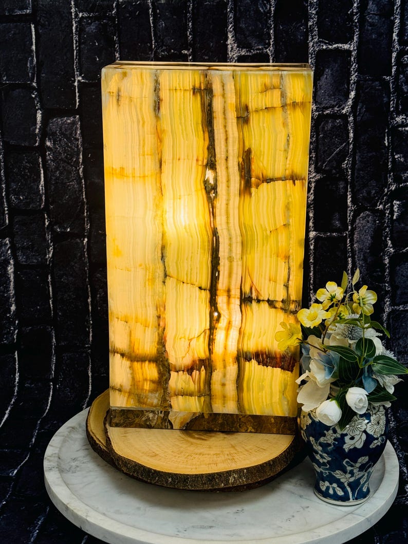 May include: A rectangular, yellow and green onyx lamp with a warm, glowing light. The lamp is sitting on a wooden base and a white marble surface.