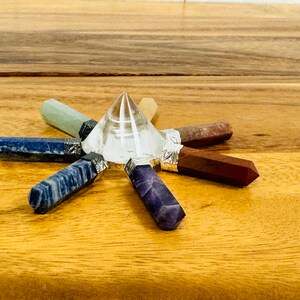 K&ouml;nnte beinhalten: Eine klare Kristallpyramide, umgeben von sieben Chakra-Kristallpunkten in einem Sternmuster. Die Kristalle sind Amethyst, Lapislazuli, blauer Aventurin, gr&uuml;ner Aventurin, Citrin, Karneol und roter Jaspis.