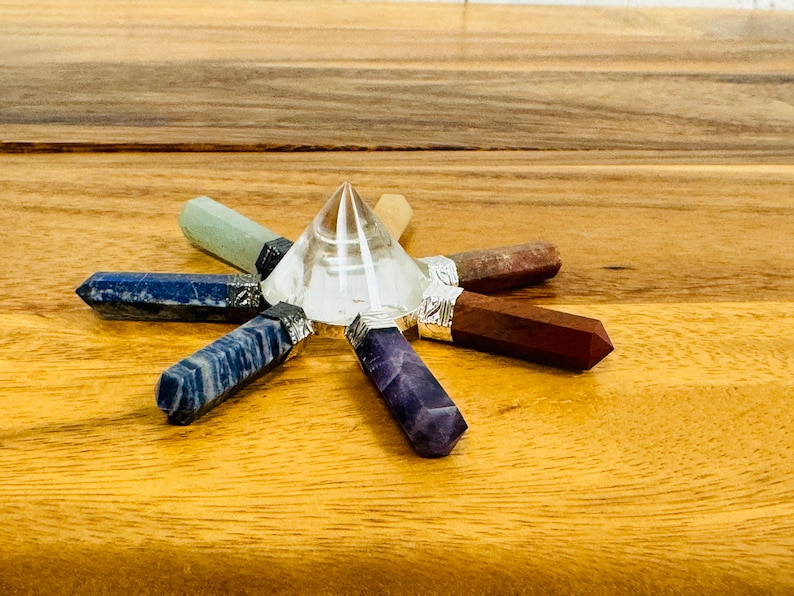 K&ouml;nnte beinhalten: Eine klare Kristallpyramide, umgeben von sieben Chakra-Kristallpunkten in einem Sternmuster. Die Kristalle sind Amethyst, Lapislazuli, blauer Aventurin, gr&uuml;ner Aventurin, Citrin, Karneol und roter Jaspis.
