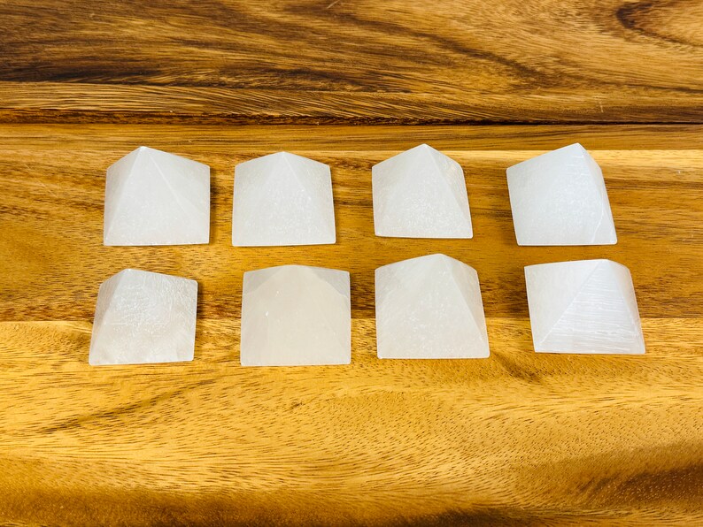 Puede incluir: Ocho pir&aacute;mides de cristal de selenita blanca dispuestas en tres filas sobre una superficie de madera.