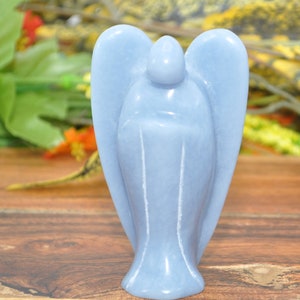 May include: A light blue angel figurine carved from a single piece of Celestite crystal. The angel has wings and a rounded head. The figurine is about 4 inches tall.