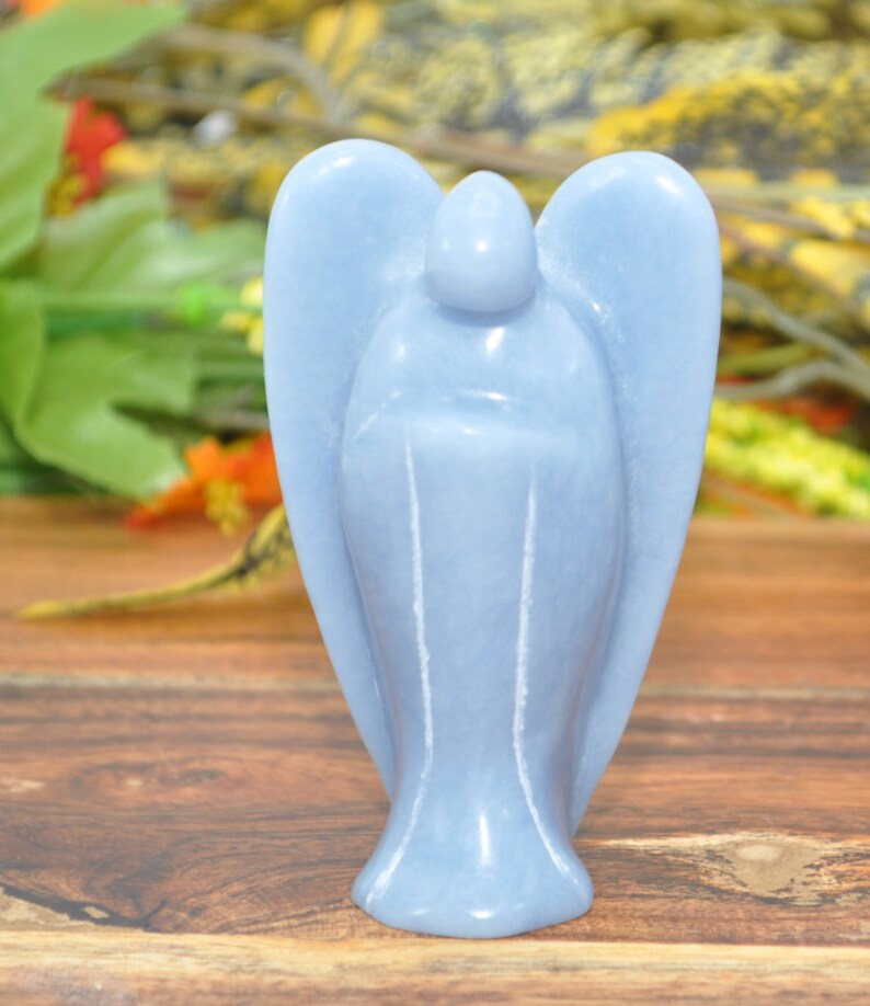 May include: A light blue angel figurine carved from a single piece of Celestite crystal. The angel has wings and a rounded head. The figurine is about 4 inches tall.