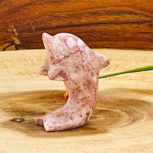 Puede incluir: Una figurita de delf&iacute;n de m&aacute;rmol rosa y blanco. El delf&iacute;n est&aacute; tallado en una pose de salto con la cola enroscada.