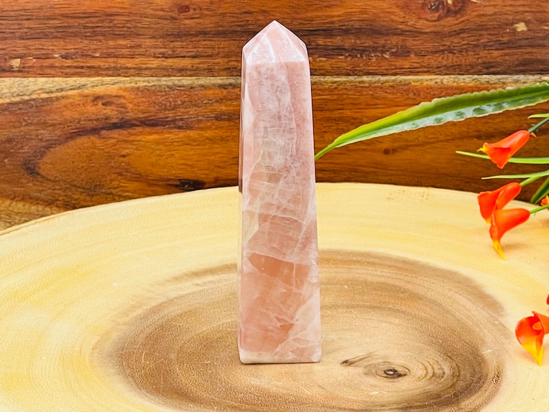 Peut inclure: Une pointe de cristal de quartz rose, &eacute;galement appel&eacute;e tour, sur une surface en bois. Le cristal est poli et a une finition lisse et vitr&eacute;e.