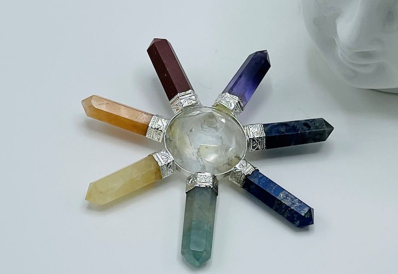 K&ouml;nnte beinhalten: Ein siebenspitziges Chakra-Set aus Kristallen mit klarem Quarz in der Mitte und Spitzen aus roten, orangefarbenen, gelben, gr&uuml;nen, blauen, indigofarbenen und violetten Kristallen.