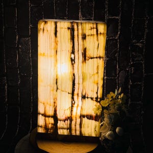 May include: A rectangular onyx lamp with a warm, yellow glow. The lamp is on a wooden base and has a natural, striped pattern.