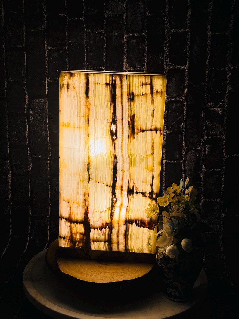 May include: A rectangular onyx lamp with a warm, yellow glow. The lamp is on a wooden base and has a natural, striped pattern.