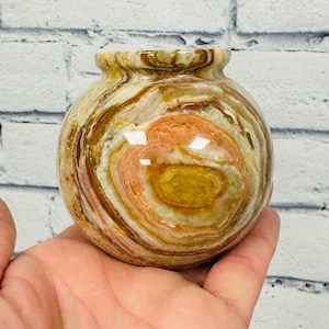 May include: A small, round, decorative vase made of onyx. The vase has a swirling pattern of brown, white, and pink.