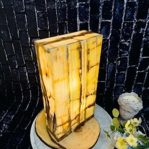 May include: A rectangular, yellow and brown onyx lamp with a warm, glowing light. The lamp is sitting on a wooden base and a white marble tray.