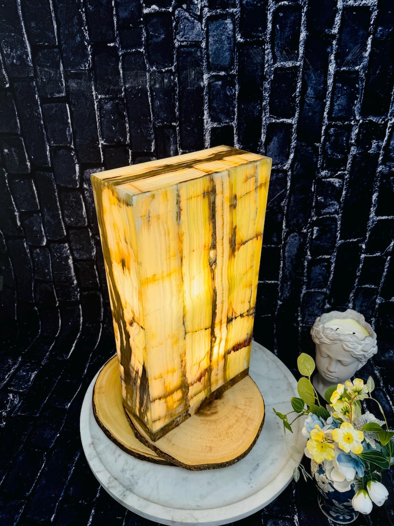 May include: A rectangular, yellow and brown onyx lamp with a warm, glowing light. The lamp is sitting on a wooden base and a white marble tray.