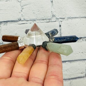 K&ouml;nnte beinhalten: Eine klare Kristallpyramide mit sieben Spitzen, jede mit einem andersfarbigen Edelstein besetzt. Die Edelsteine sind braun, gelb, gr&uuml;n, blau und lila.