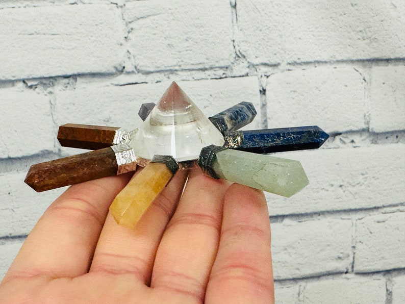 K&ouml;nnte beinhalten: Eine klare Kristallpyramide mit sieben Spitzen, jede mit einem andersfarbigen Edelstein besetzt. Die Edelsteine sind braun, gelb, gr&uuml;n, blau und lila.