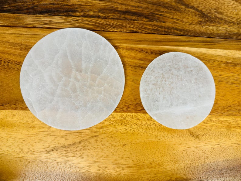 May include: Two white selenite charging plates of different sizes on a wooden surface.