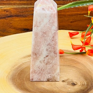 Peut inclure: Une pointe de cristal rose et blanche, &eacute;galement appel&eacute;e ob&eacute;lisque de cristal, repose sur une surface en bois. Le cristal a une finition lisse et polie et est en forme de pyramide.