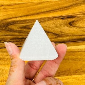 May include: A white selenite pyramid crystal, a type of mineral known for its calming and purifying properties.
