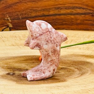 Puede incluir: Una figurita de delf&iacute;n de m&aacute;rmol rosa y blanco. El delf&iacute;n est&aacute; tallado en una pose de salto con la cola enroscada.