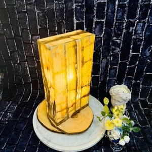 May include: A rectangular, yellow and brown onyx lamp with a warm, glowing light. The lamp is sitting on a wooden base and a white marble tray.