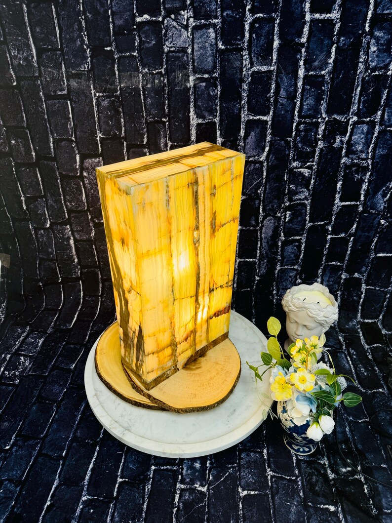 May include: A rectangular, yellow and brown onyx lamp with a warm, glowing light. The lamp is sitting on a wooden base and a white marble tray.