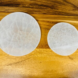 May include: Two white selenite charging plates of different sizes on a wooden surface.