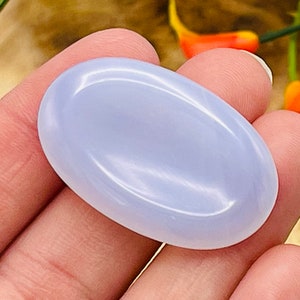 May include: A smooth, oval-shaped blue chalcedony gemstone. The stone is polished and has a light blue color.