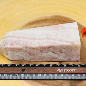Peut inclure: Une pointe de cristal ray&eacute;e rose et blanche, d'environ 18 cm de long, reposant sur une surface en bois.