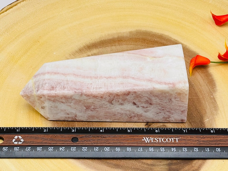 Peut inclure: Une pointe de cristal ray&eacute;e rose et blanche, d'environ 18 cm de long, reposant sur une surface en bois.