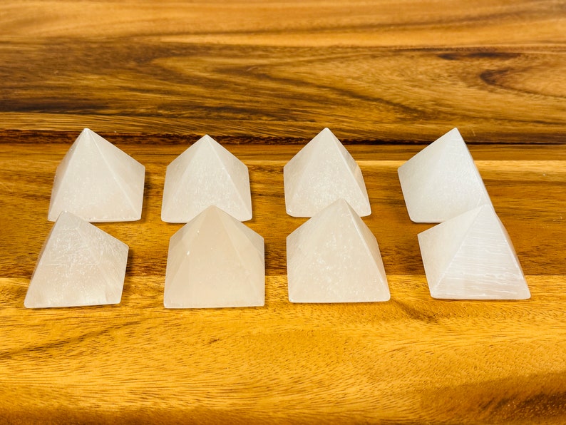 May include: Eight white selenite crystal pyramids arranged in two rows of four on a wooden surface.