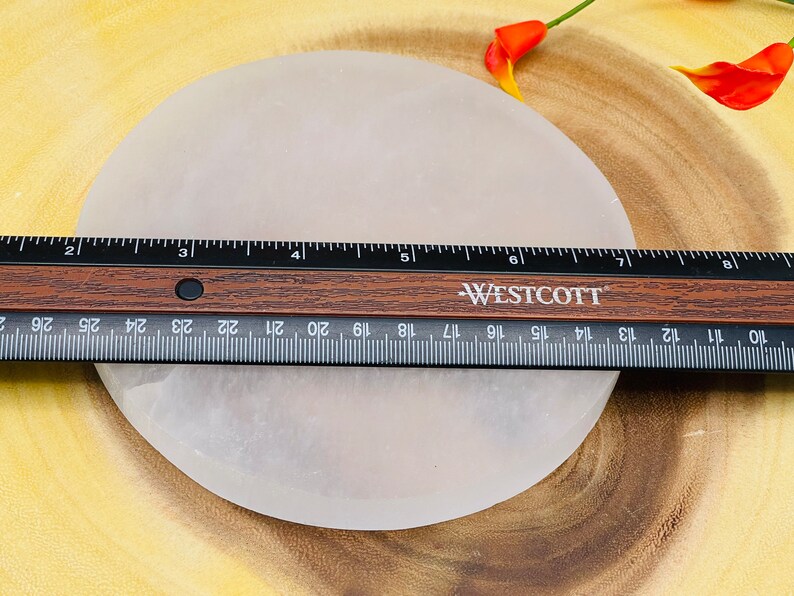 May include: A white selenite charging plate, approximately 7 inches in diameter, is shown on a wooden surface. A ruler is placed on top of the plate to show its size.