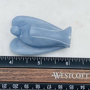 May include: A light blue angel figurine carved from a smooth, polished stone. The angel is lying on its back with its wings spread out. The figurine is about 4 inches long.