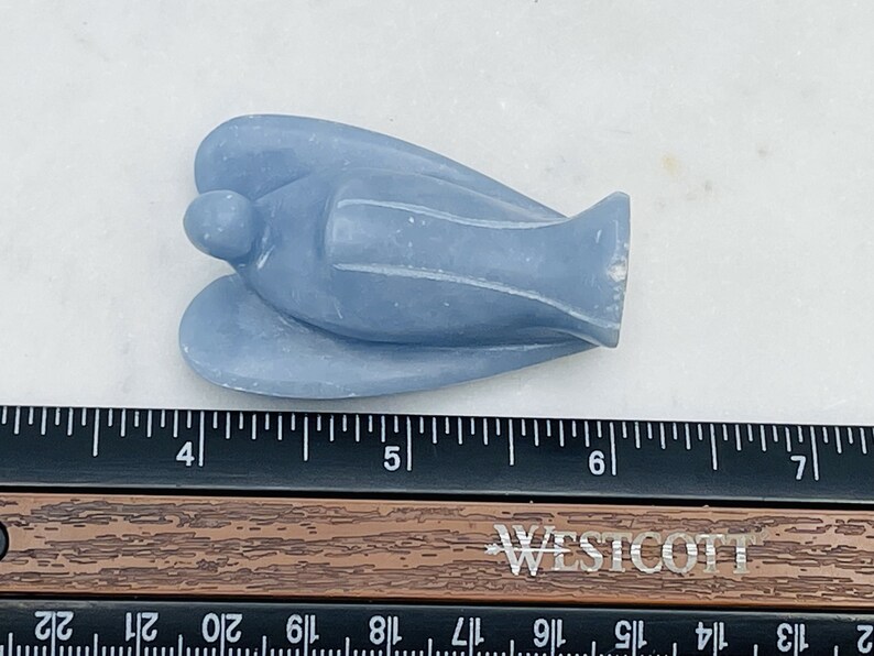 May include: A light blue angel figurine carved from a smooth, polished stone. The angel is lying on its back with its wings spread out. The figurine is about 4 inches long.