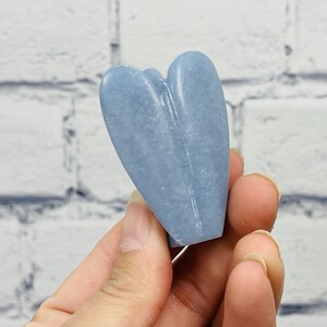 May include: A light blue heart-shaped crystal, carved from a natural stone. The crystal is smooth and polished, with a subtle sheen.