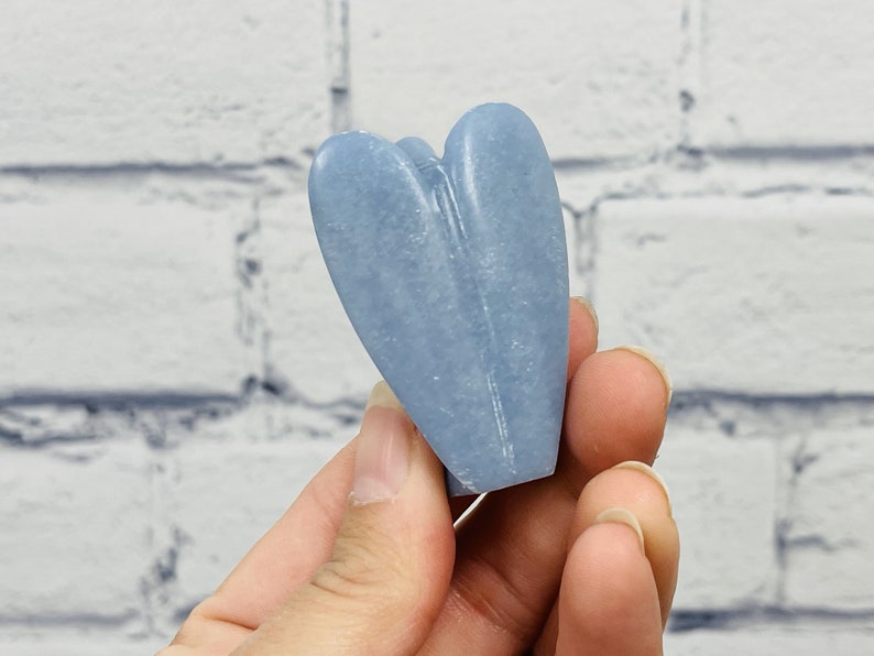 May include: A light blue heart-shaped crystal, carved from a natural stone. The crystal is smooth and polished, with a subtle sheen.