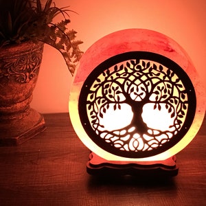 May include: A pink Himalayan salt lamp with a carved tree of life design. The lamp is lit and casting a warm glow.