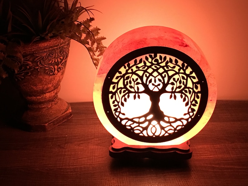May include: A pink Himalayan salt lamp with a carved tree of life design. The lamp is lit and casting a warm glow.