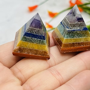 May include: Two small, layered, multi-colored crystal pyramids. The pyramids are made of seven different colors of crystals, including amethyst, lapis lazuli, green aventurine, citrine, yellow tiger's eye, carnelian, and red jasper.