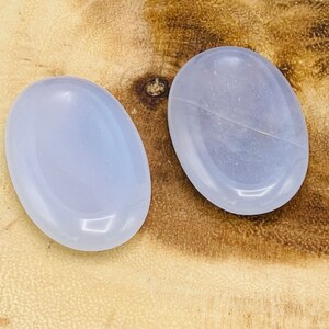 May include: Two smooth, oval-shaped, light blue stones on a wooden surface.