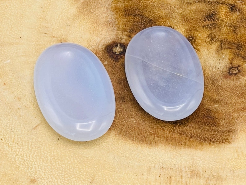 May include: Two smooth, oval-shaped, light blue stones on a wooden surface.